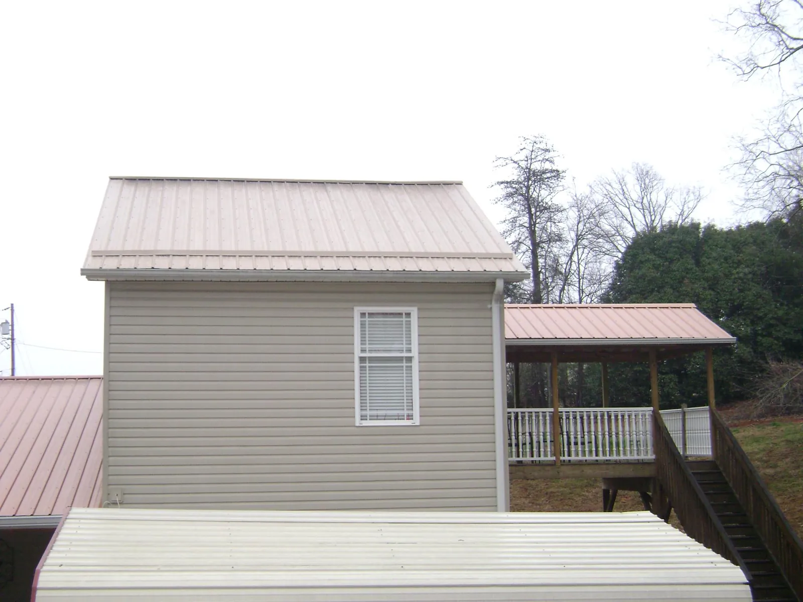Tan metal roofs on a two story addition and attached porch, from a Roof Replacement job in Bowling Green